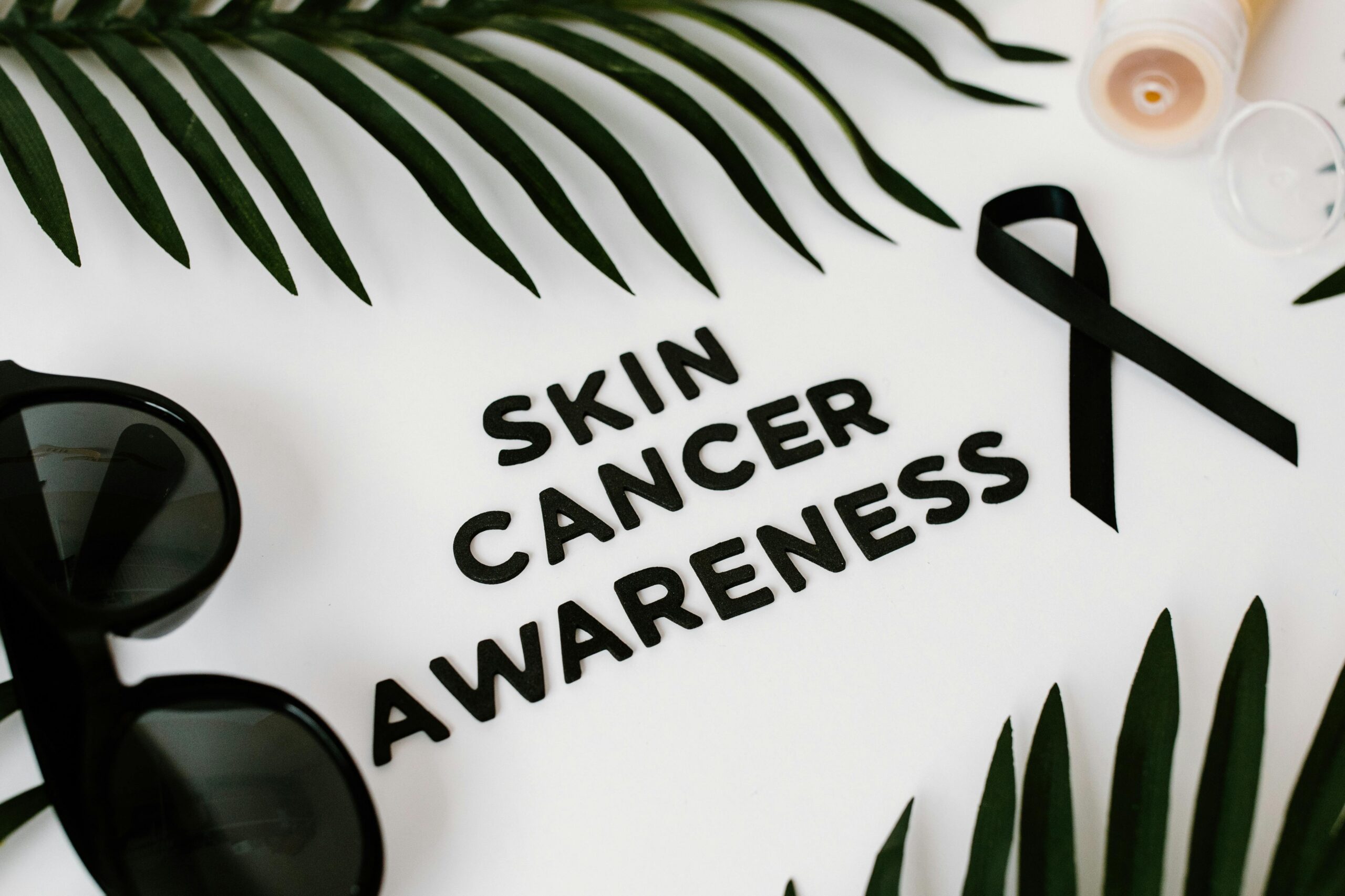 Still life composition promoting skin cancer awareness featuring a black ribbon and sunglasses.